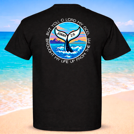 Black t-shirt with a whale and ocean design on the back, set against a beach background.