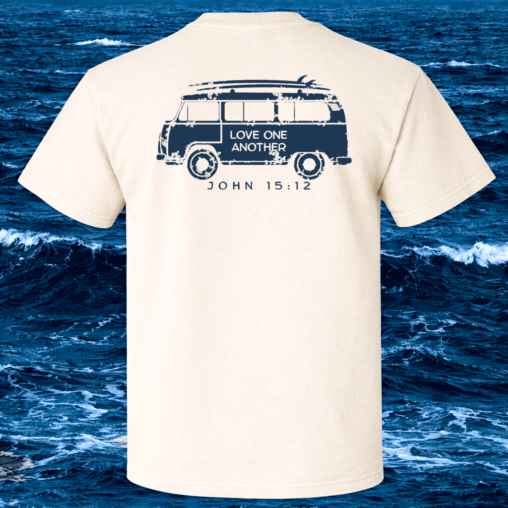 Beige t-shirt with a graphic of a VW van and text on the back, displayed against a backdrop of ocean waves.