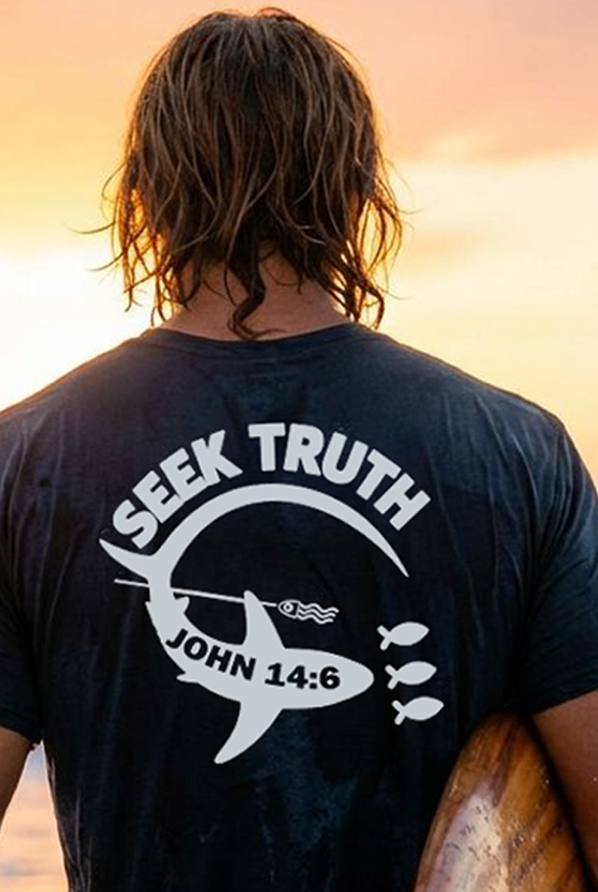 Person wearing a black t-shirt with 'Seek Truth' and 'John 14:6' text, holding a surfboard at sunset.
