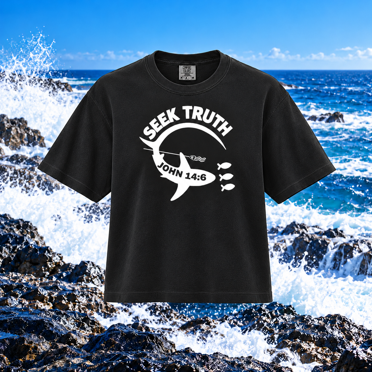 A black short-sleeve graphic T-shirt with a white shark design and the text 'SEEK TRUTH JOHN 14:6' on the front, shown against a rocky ocean background with waves crashing.