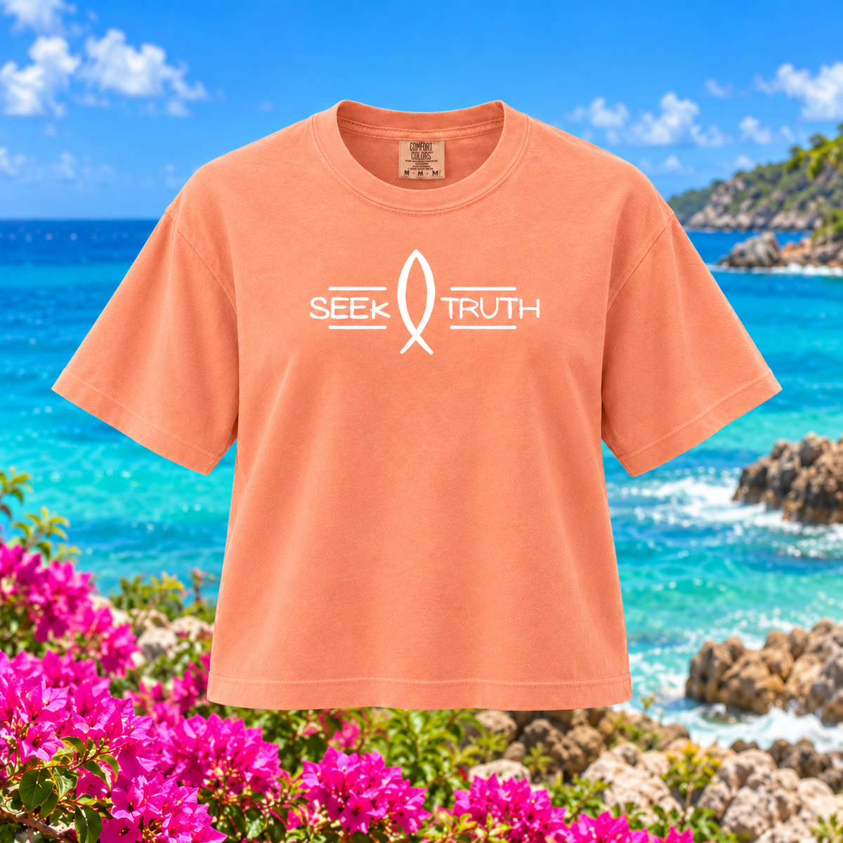 A peach-colored short-sleeve t-shirt with a white 'SEEK TRUTH' ribbon graphic on the chest, displayed against a vibrant beach and flower background.