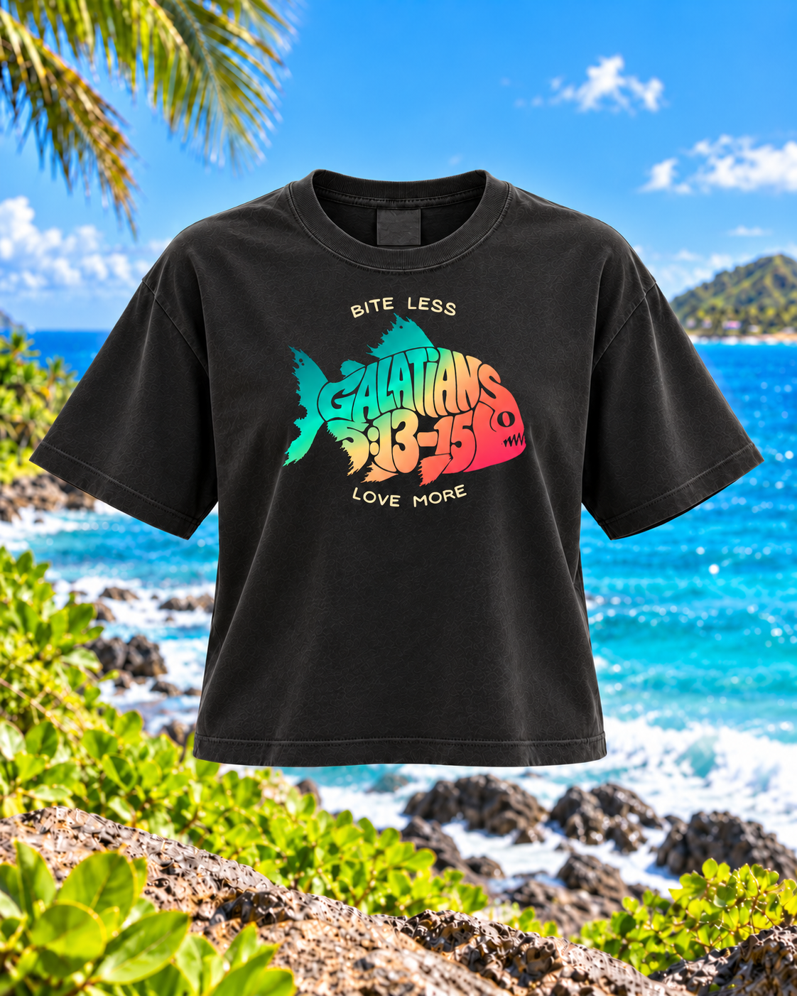 A black short-sleeve graphic T-shirt displayed against a tropical beach backdrop. The shirt features a colorful fish graphic with the words 'GALACTICS 13-15' and 'BITE LESS LOVE MORE'.