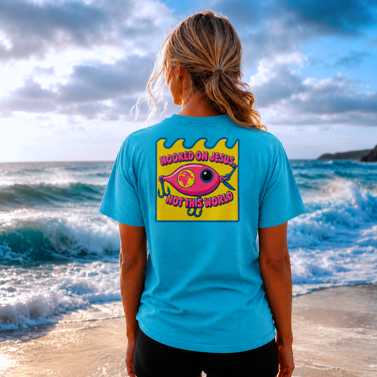 Female model wearing a Lagoon Blue Comfort Colors 1717 T-shirt featuring the Pink Fishing Lure Hooked on Jesus coastal Christian graphic by Seek Truth Graphics.