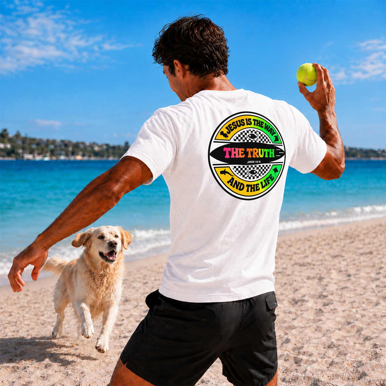Man playing with a dog on a beach, wearing a white t-shirt with a graphic design.