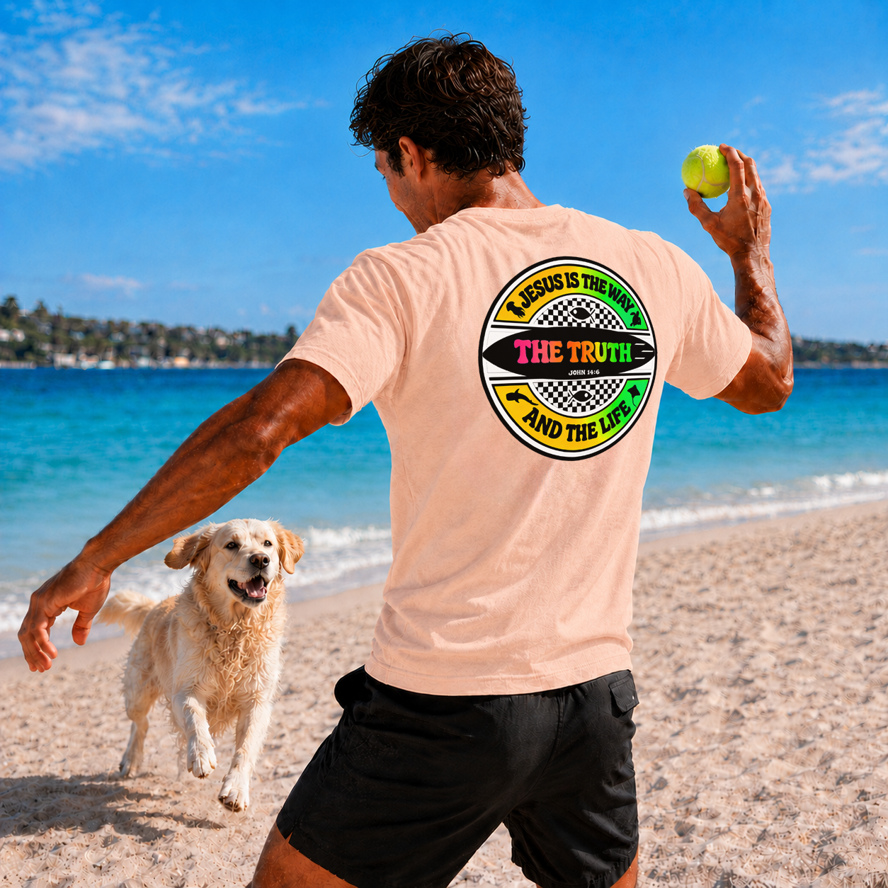 Man playing with a dog on a beach, wearing a t-shirt with a graphic design.