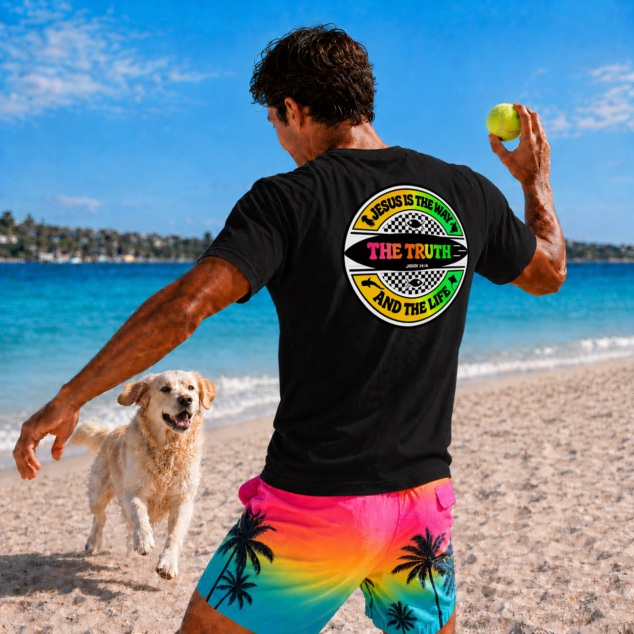Man playing with a dog on a beach, wearing a black t-shirt with a colorful graphic and text.