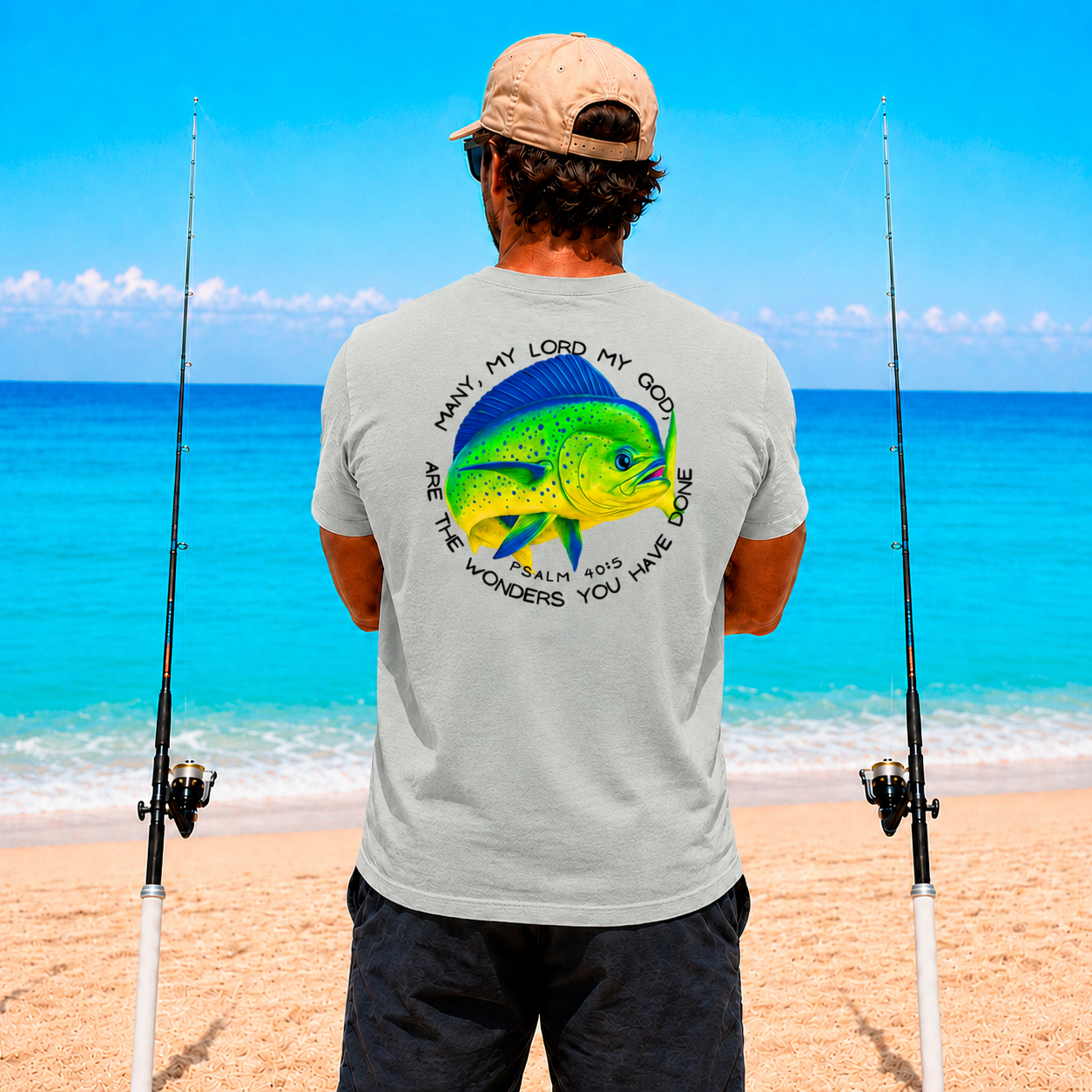 Man on a beach with fishing rods, wearing a t-shirt with a fish design and text.