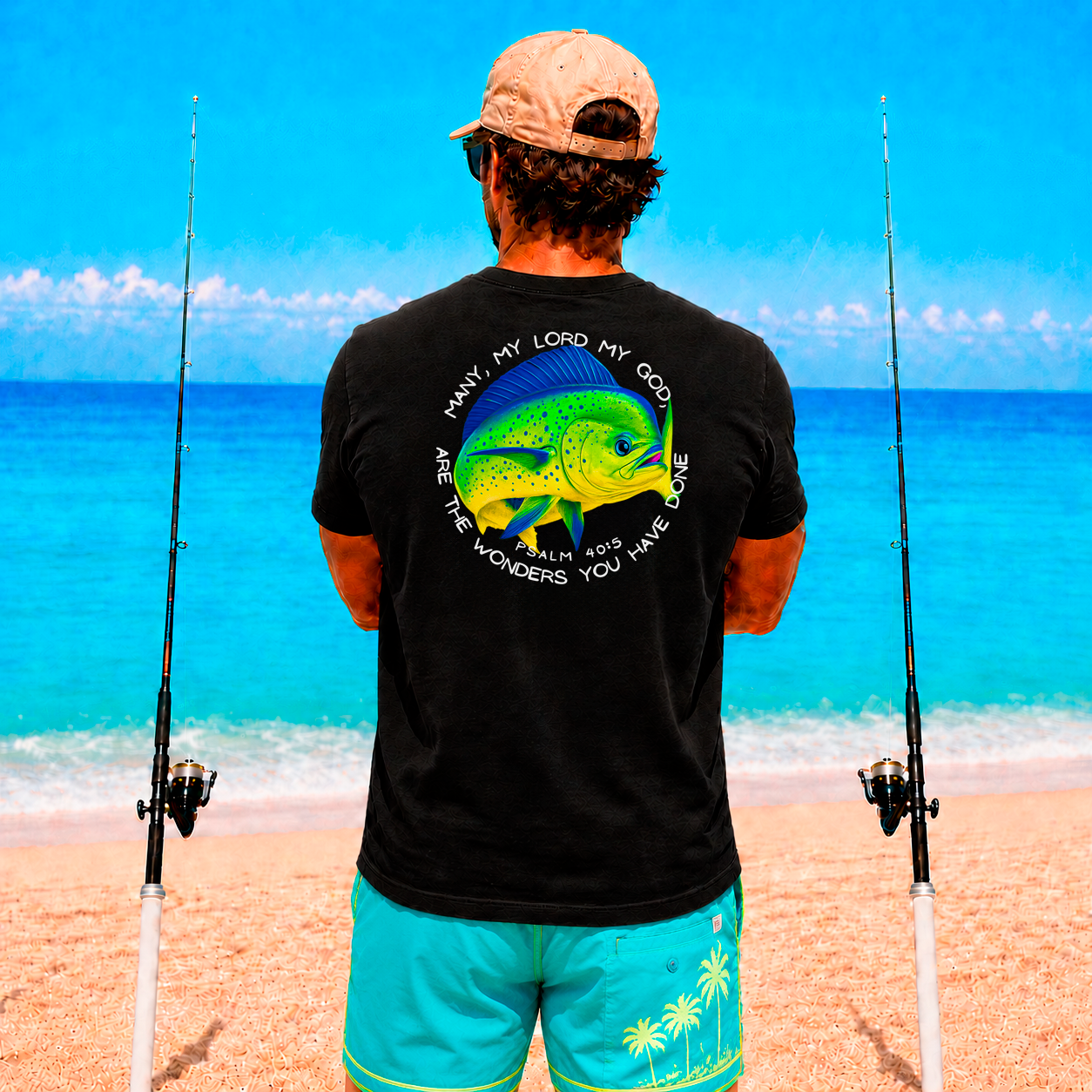 Man on a beach holding two fishing rods, wearing a black t-shirt with a Mahi Mahi fish design and text.