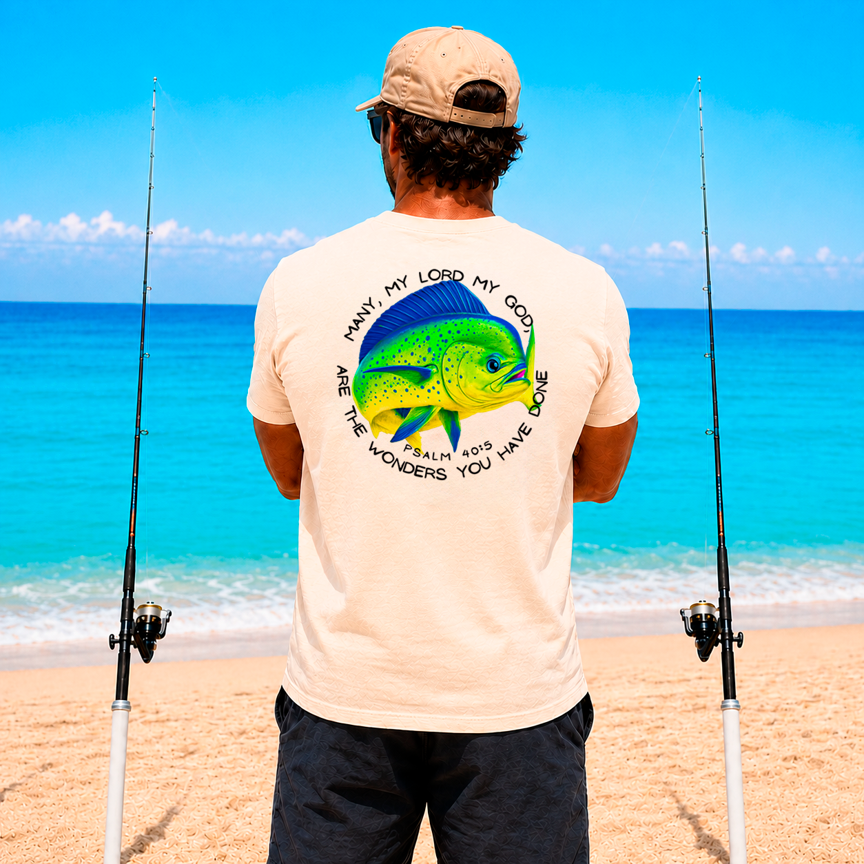 Man on a beach with fishing rods, wearing a t-shirt with a fish design and text.