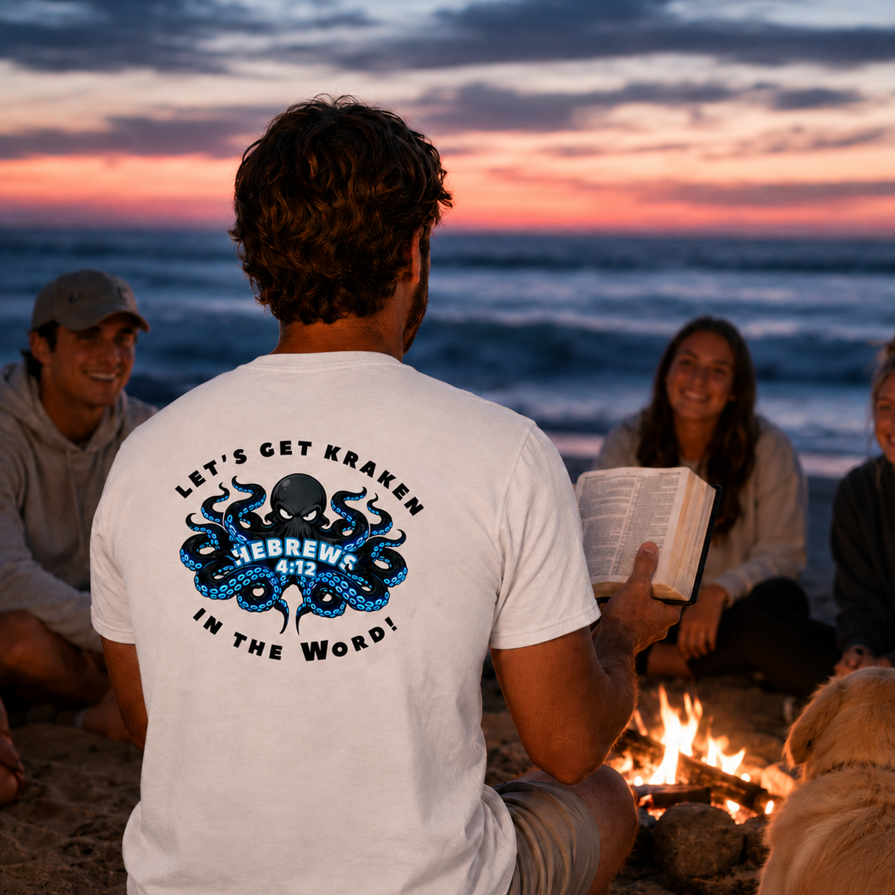 Group of people sitting around a campfire on the beach at sunset, with one person wearing a white t-shirt with a graphic design.