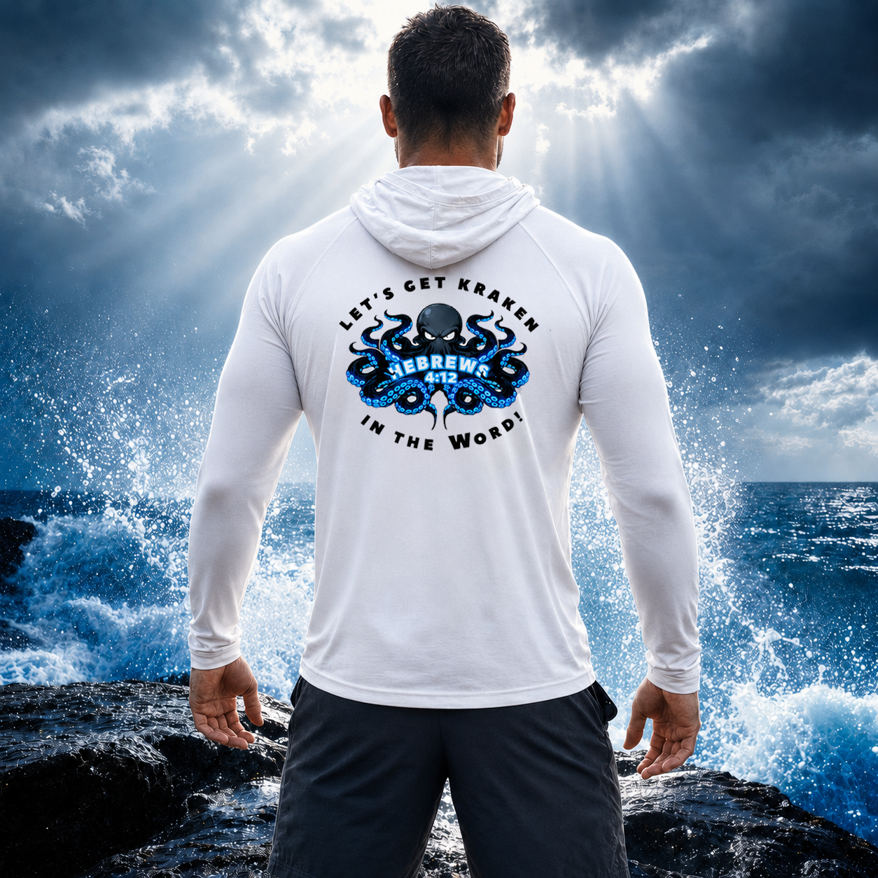 Person wearing a white hoodie with a graphic design on the back, standing on rocks with ocean waves and sky in the background.