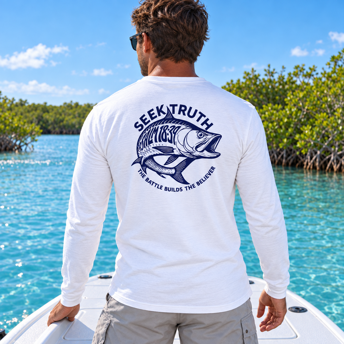 A man wearing a white long-sleeve t-shirt with a navy blue fish graphic and the text 'SEEK TRUTH' on the back, standing on a boat with turquoise water and mangroves in the background.