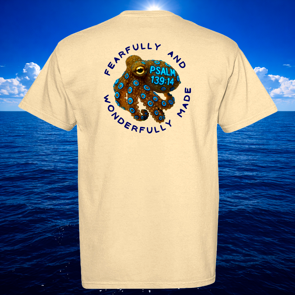 Beige t-shirt with an octopus graphic and text on the back, against a blue ocean and sky background.