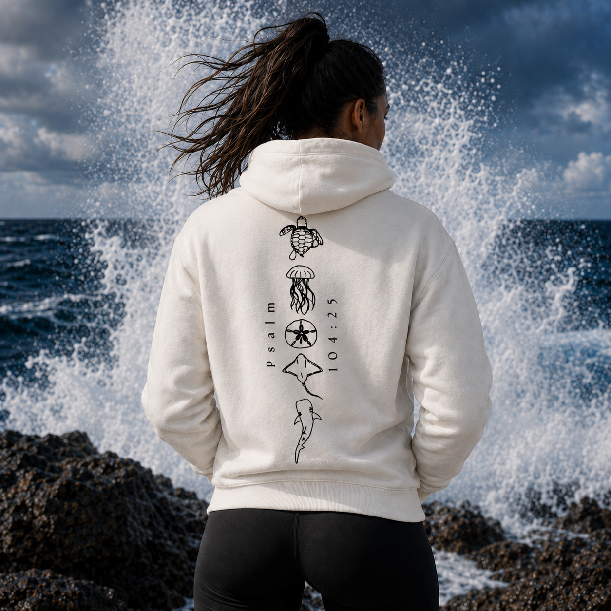 Person wearing a white hoodie with ocean-themed designs by the sea