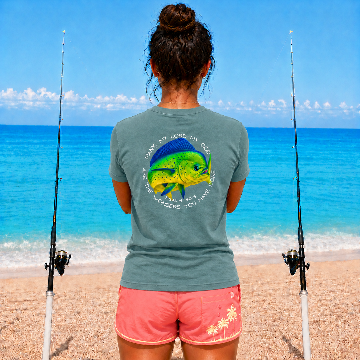 Person on a beach with fishing rods, wearing a t-shirt with a Mahi fish design.
