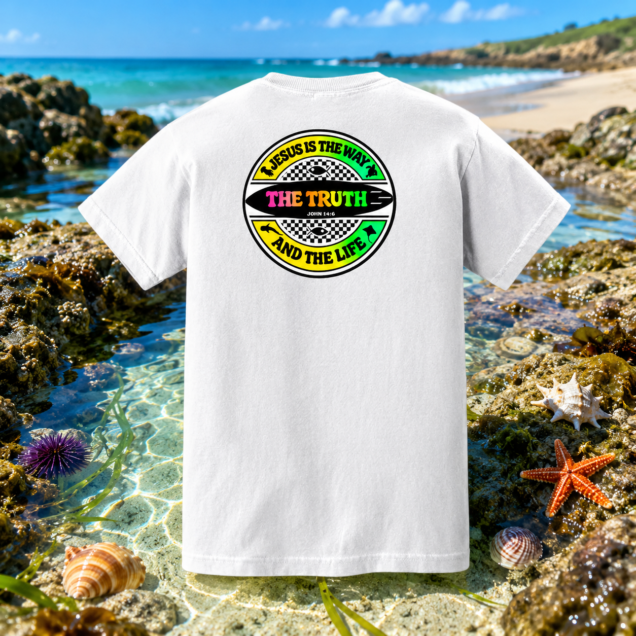 White t-shirt with a colorful graphic on a beach with ocean and rocks in the background
